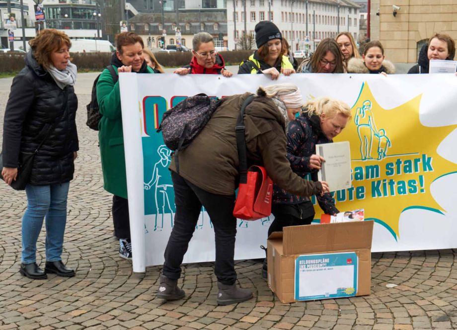 Kita-Beschäftigte vor dem Hessischen Staatsarchiv eine große Kiste voller Bildungspläne, die mangels
