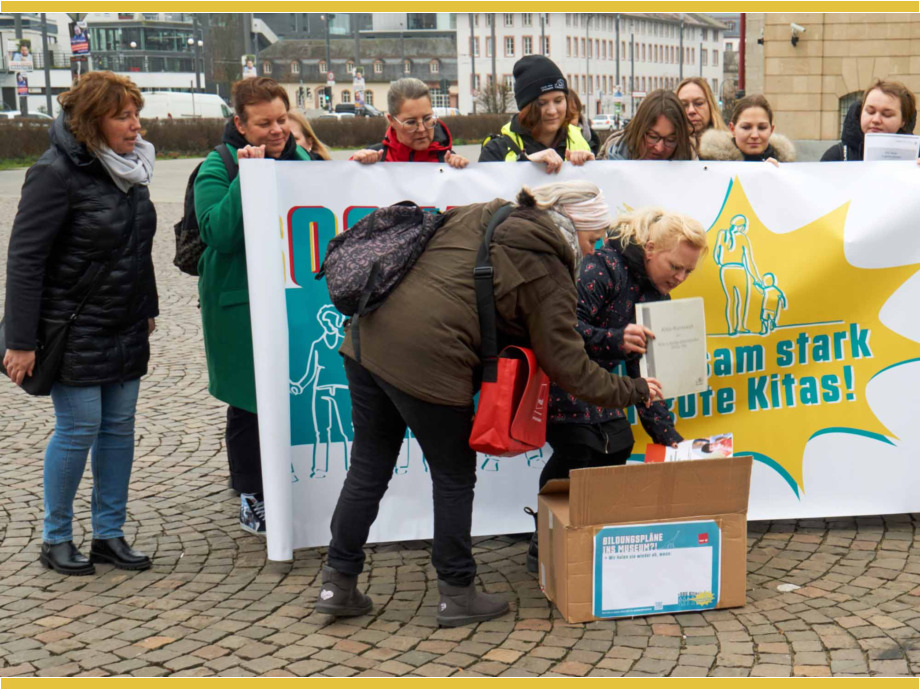 Kita-Beschäftigte vor dem Hessischen Staatsarchiv eine große Kiste voller Bildungspläne, die mangels